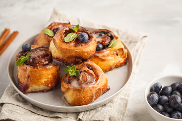 Homemade cinnamon buns with blueberries and cinnamon on gray plate, breakfast white background