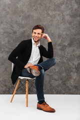 Cheerful young businessman sitting over grey wall