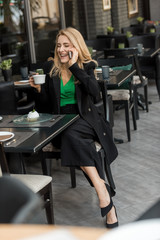 smiling woman with cup of coffee talking on smartphone in cafe