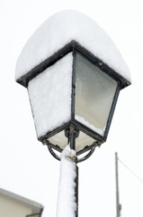 Pile of snow on street lamp, vertical with white sky on snowfall