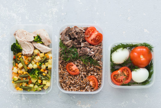 Diet food in the three containers on a gray background. Boiled and fresh vegetables, buckwheat, eggs, beef, chicken.
