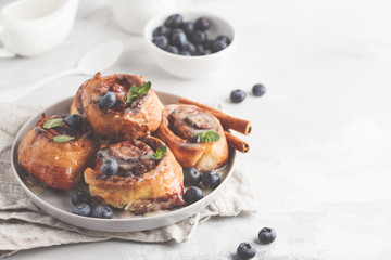 Homemade cinnamon buns with blueberries and cinnamon on gray plate, breakfast white background, copy space