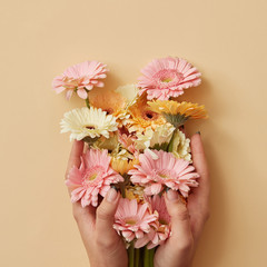 The girl's hands hold a beautiful bouquet of gerberas on a yellow paper background.