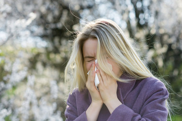 Girl blows his nose in a handkerchief against a backdrop of a blooming garden. The concept of an...