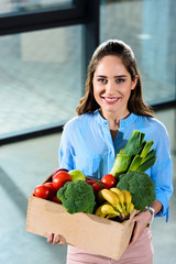 Smiling woman holding box with fresh fruits and vegetables