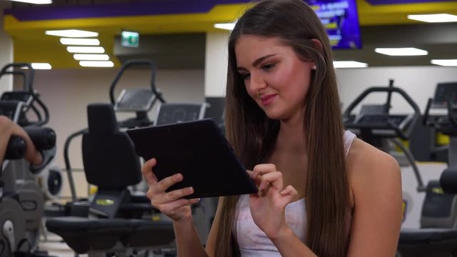 A young beautiful woman works on a tablet in a gym - closeup
