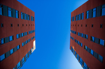 Two houses in front of each other. Photo take from low angle; two red suburban buildings facing eachother with blue sky in background. Suburban and building concept. - Powered by Adobe