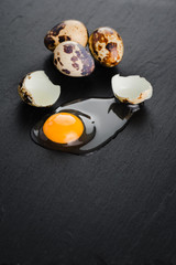 Quail eggs on black stone background, broken, cracked quail egg, yolk of quail egg. Organic product.