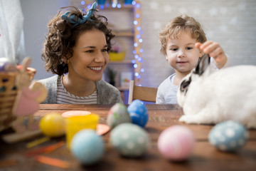 Portrait of little boy playing with cute fluffy bunny on Easter day while celebrating at home with mom