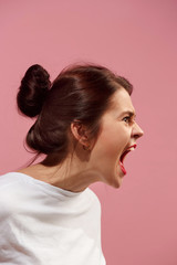The young emotional angry woman screaming on pink studio background