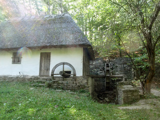 Ukraine, Pyrohiv (Kiev) - September 17, 2017: An abandoned old rural house - a water mill with white walls, thatched roof and two wooden wheels in the facade in the forest © ioanna_alexa