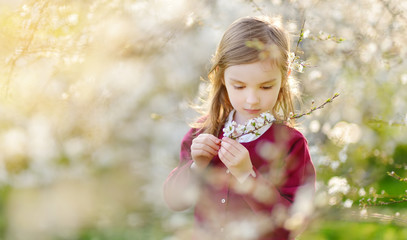 Adorable little girl in blooming cherry tree garden on beautiful spring day