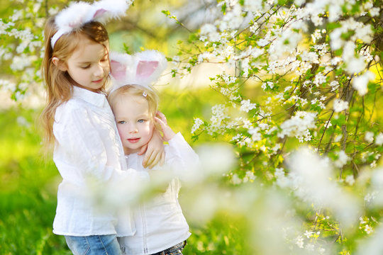 Two adorable little sisters wearing bunny ears in a spring garden on Easter day
