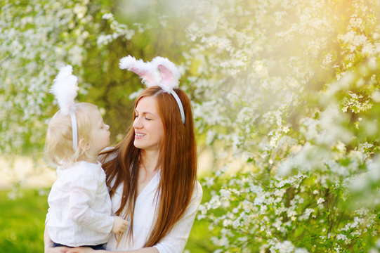Young mother and her daughter wearing bunny ears in a spring garden on Easter day