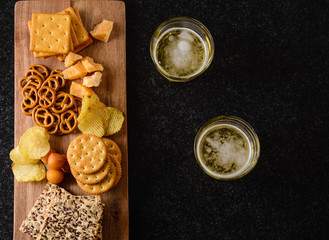 Light beer with a snack of chips, nuts and chesee on a black background.