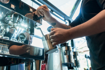 High angle view close-up of the hand of a barista holding a stainless mug while using a modern coffee machine