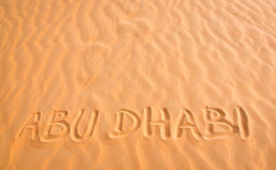 Fototapeta na wymiar Abu Dhabi handwritten text in desert sand.