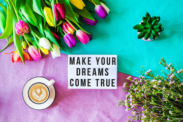 Make your dreams come true written in lightbox with spring flowers from above