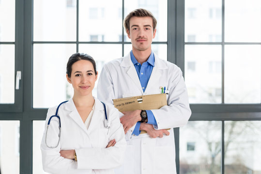 Portrait of two determined physicians wearing white medical gowns while looking at camera with serious facial expression in a modern health center