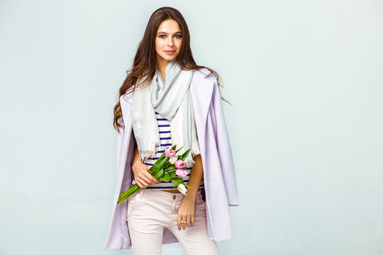 Fashion photo of a beautiful young woman with tulips in her hand .she dressed in a beautiful coat, scarf, pants and T-shirt with stripes.Spring concept. March 8. beautiful girl in stylish clothes

