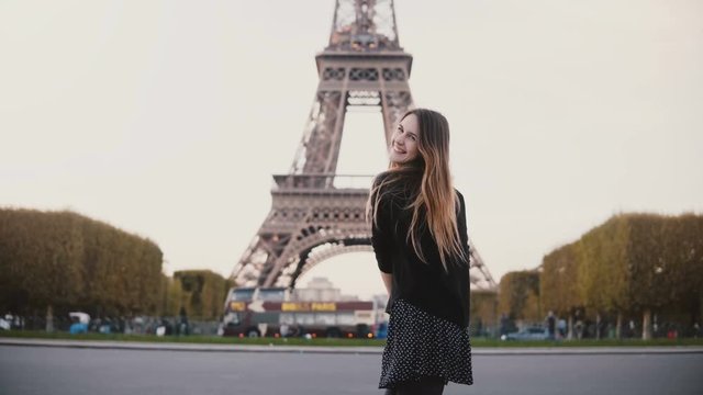 Happy young woman feeling joy because of seeing Eiffel tower in Paris, France. Girl smile at camera and send blow kiss.