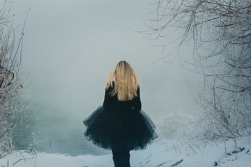 blonde girl in a black puffy skirt stands back in the snowy woods