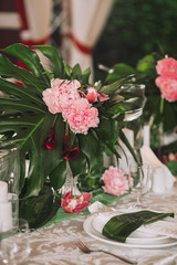 A beautiful served table with plates for a dinner party decorated with leaves of a palm tree, white candles and flowers of a orchid