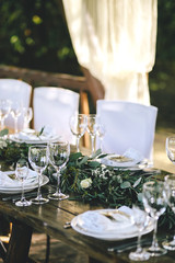 Decorated elegant wooden wedding table in rustic style with eucalyptus and flowers, porcelain plates, glasses and chairs