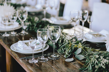 Decorated elegant wooden wedding table in rustic style with eucalyptus and flowers, porcelain plates, glasses, napkins and cutlery - Powered by Adobe