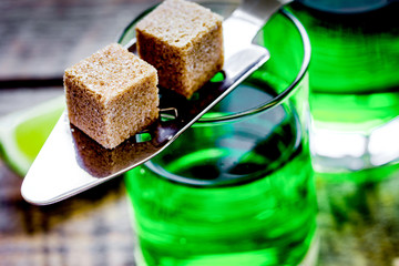 absinthe with sugar cubes in spoon on wooden background