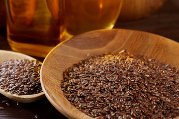 Flax seeds in bowl and flaxseed oil in glass bottle on wooden background, top view, close-up, selective focus
