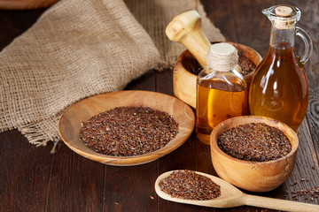 Flax seeds in bowl and flaxseed oil in glass bottle on wooden background, top view, close-up, selective focus