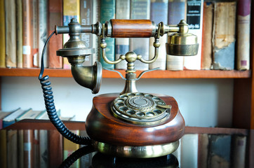 Old wire telephone decorated in library with blurred book on shelf in the background