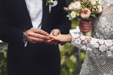 Stylish groom puts a wedding ring on brides finger.  - 193958372