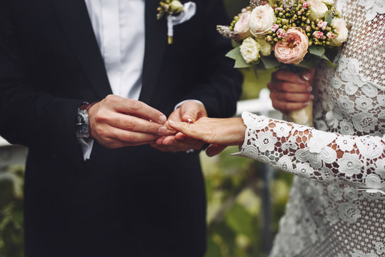 Stylish groom puts a wedding ring on brides finger. 