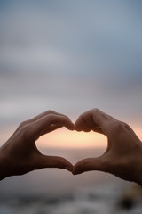 Obraz premium Bright sunset and hands of a man forming a heart shape silhouette on natural oudoors abstract background. Close up on emotional human feeling, over sunny seascape shore leisure travel landscape