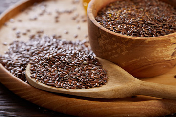 Flax seeds in wooden bowl and spoon on rustic wooden background, top view, shallow depth of field