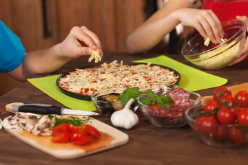 Kids making a pizza at home - putting the grated cheese on