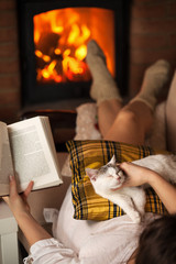 Woman relaxing at the fireplace with a book and her kitten