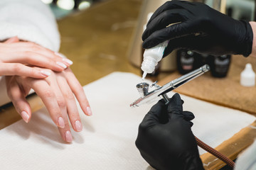 Closeup shot of a woman in a nail salon receiving a manicure by a beautician with airbrush. Woman getting nail manicure.