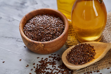 Flax seeds in bowl and flaxseed oil in glass bottle on wooden background, top view, close-up, selective focus