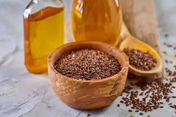 Flax seeds in bowl and flaxseed oil in glass bottle on wooden background, top view, close-up, selective focus