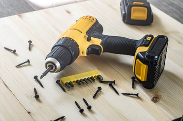 yellow screwdriver on a wooden table, screws, a set of bits.