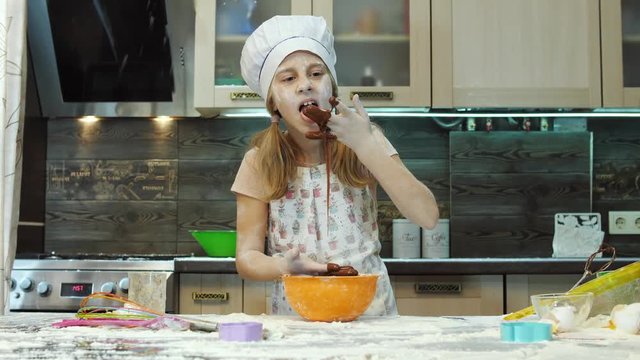Pretty kid having fun in the kitchen play and mixing chokolate dough with hands.
