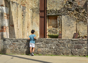 Fototapeta na wymiar The boy looks at the ruined building during World War 2 in Oradour sur Glane France