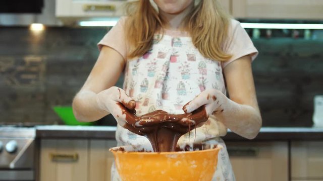 Pretty kid having fun in the kitchen play and mixing chokolate dough with hands.