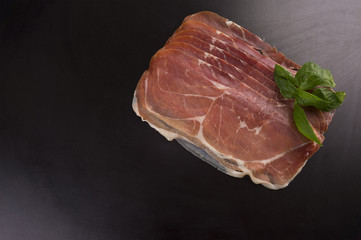 Prosciutto. Smoked pork rashers with basil on black background. Top view with copy space for text.