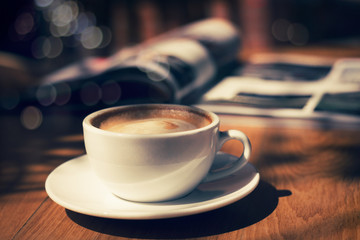 cup of coffee with magazine on table in cafe in dark tone and vintage .