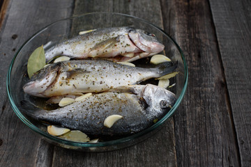 Dorado fish on a glass dish for baking, wooden background