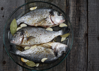 Dorado fish on a glass dish for baking, wooden background